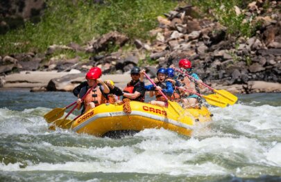 A family with older children splash through a rapid on the Green River through Split Mountain Canyon during a rafting trip with OARS in 2025.