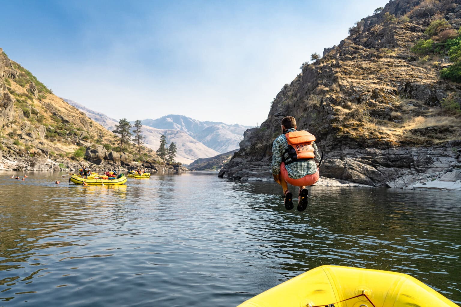 A man doing a cannonball off of a yellow raft into the river