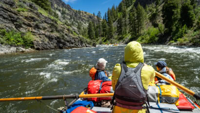 A guide rowing an oar raft down a scenic river with two guests in front as passengers
