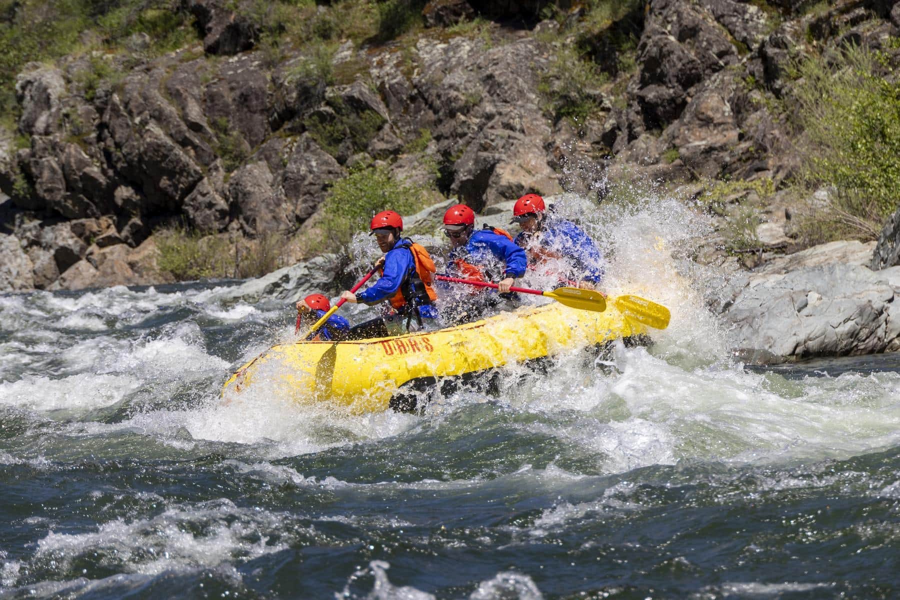 A group of paddlers in a yellow raft hit a splashy wave on a river sideways