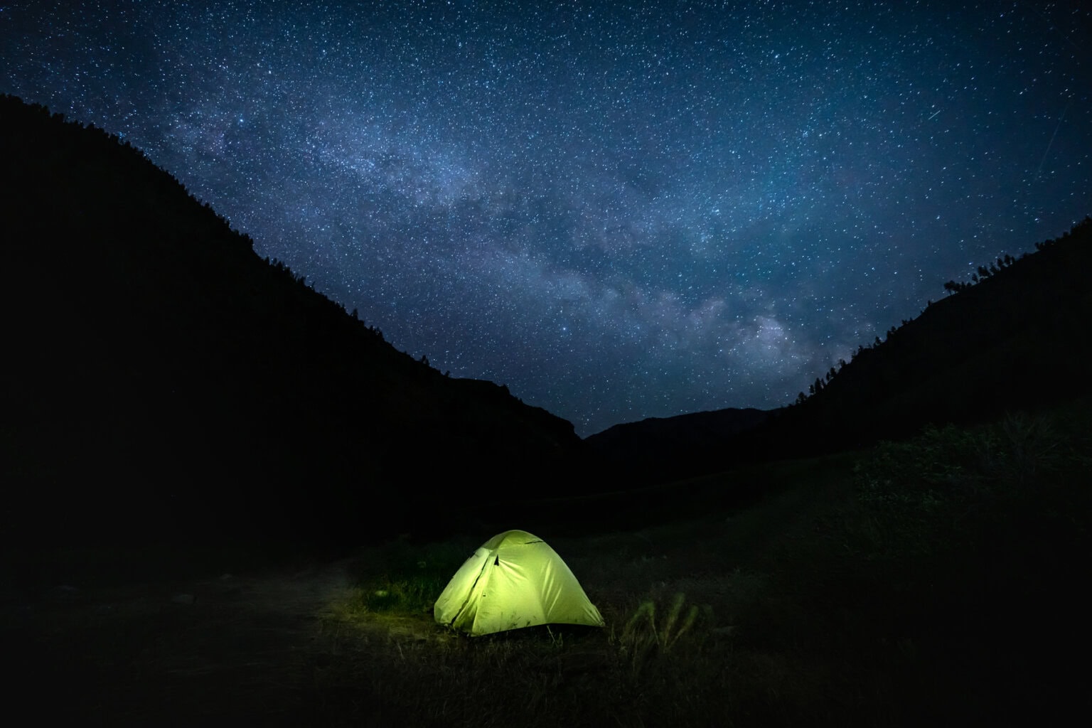 A tent lit up with a starry night sky above