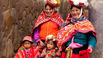 Two Peruvian women and two children adorned with Peruvian hand-crafted clothing and knit blankets pose for a photo.