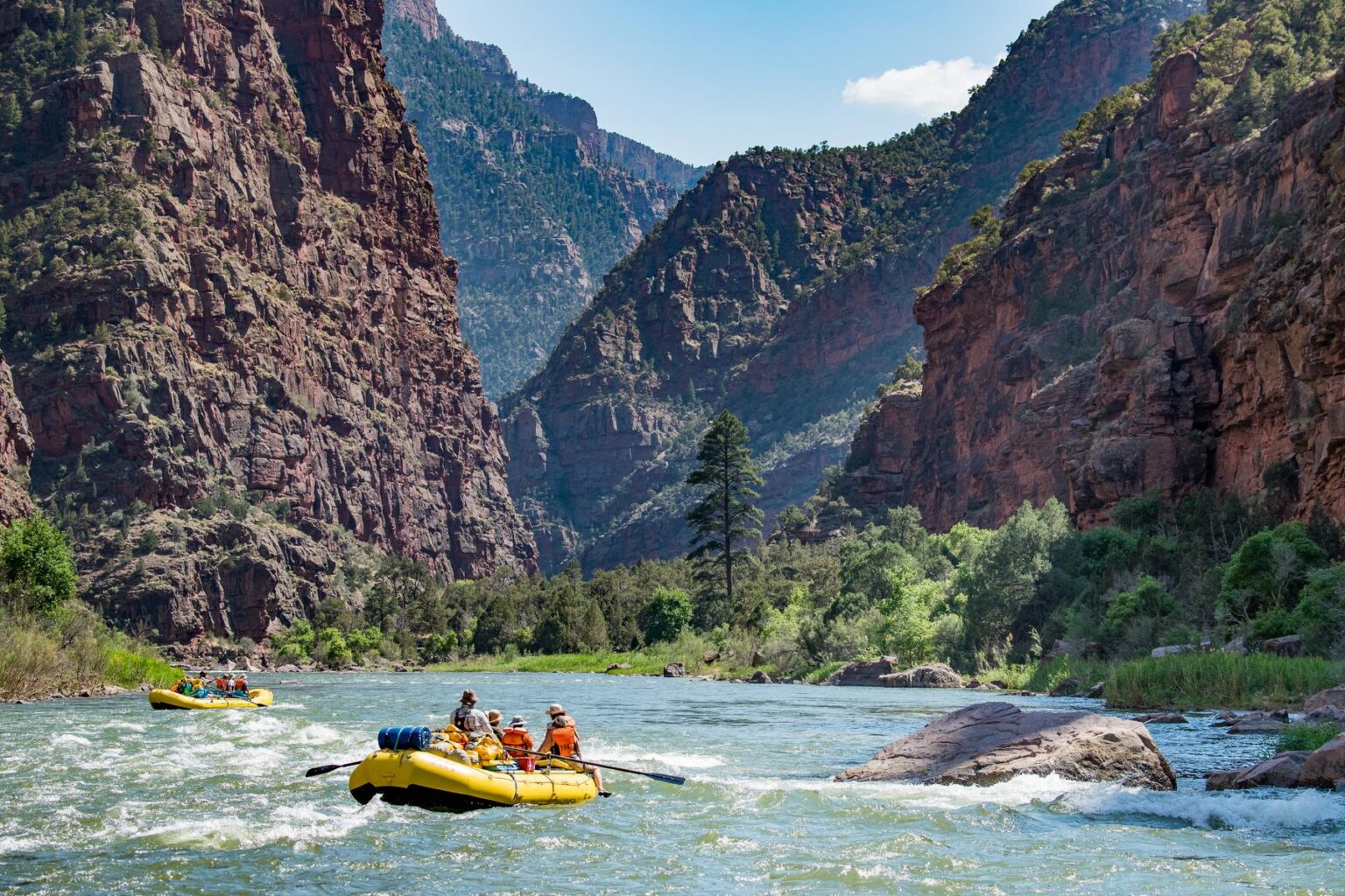 A yellow raft floats down a river toward a winding red rock canyon