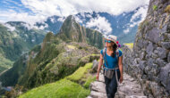 A woman wearing a traditional Peruvian hat hikes up rock steps high above Machu Picchu.