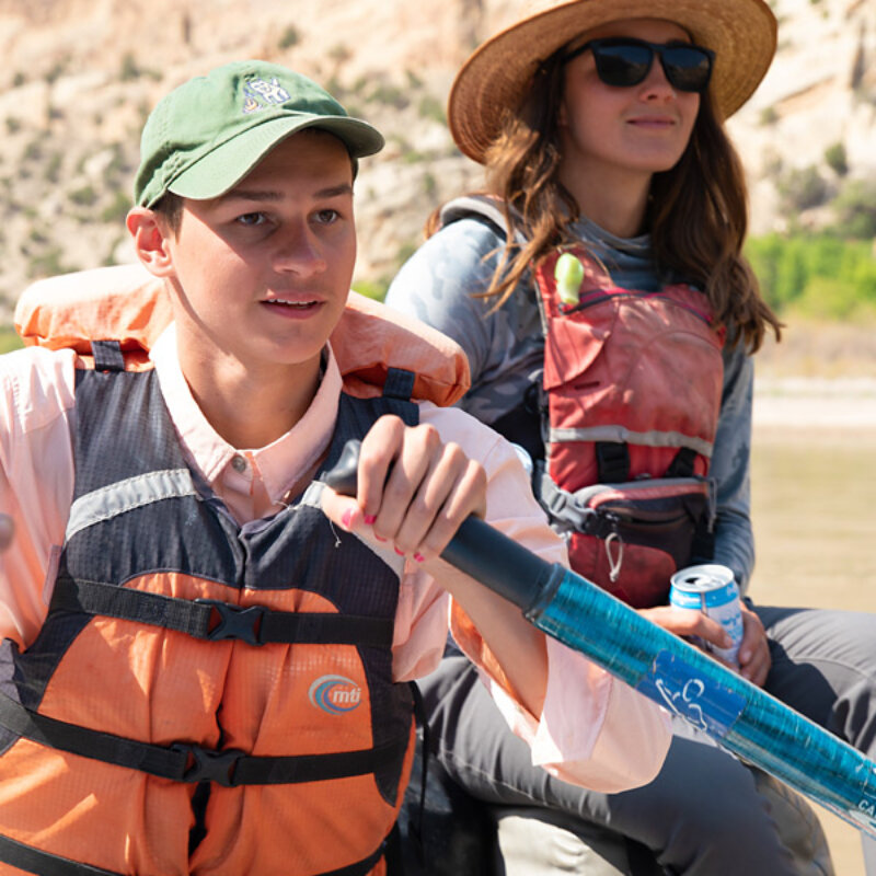 A young boater in training rows while a training guide sits behind them.