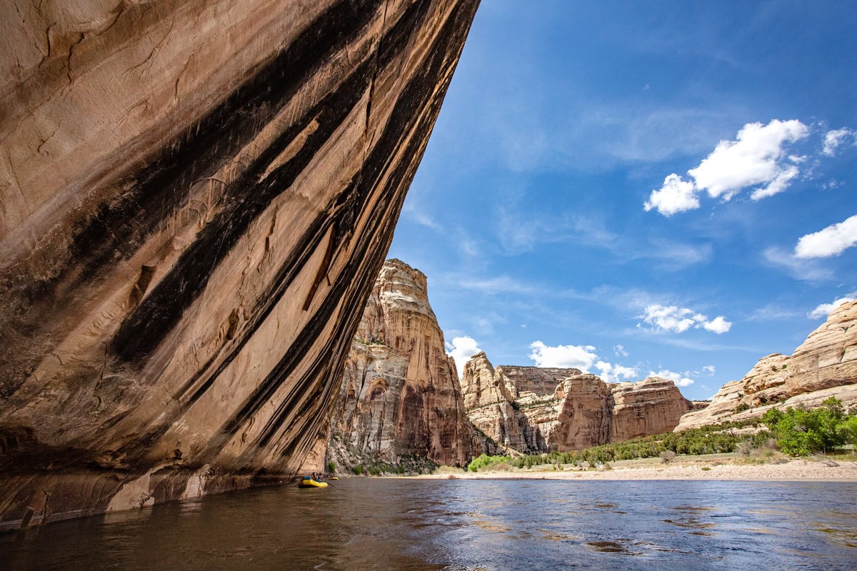 A yellow raft floats past a massive sandstone wall in the Yampa River Canyon