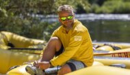 A photo of an OARS guide in a sun hoody, sitting on a raft near the American River
