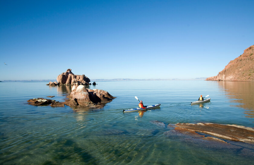 Two sea kayakers glide thorugh blue water in Baja Mexico.