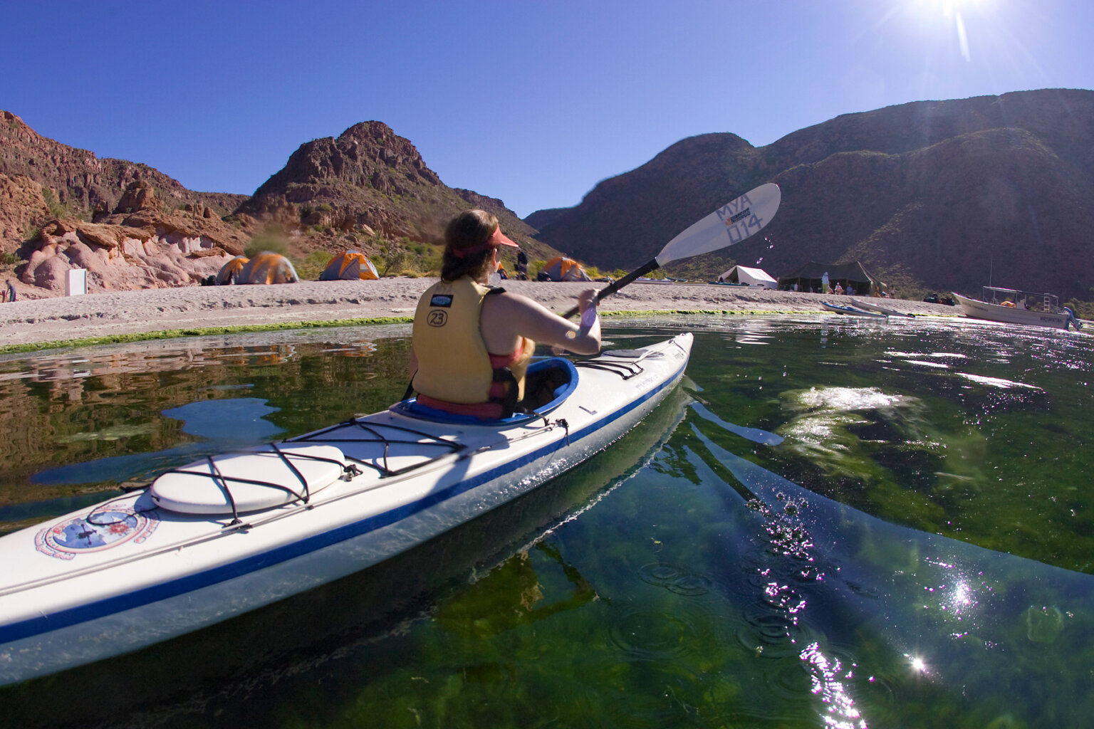 A kayaker paddles back to the shoreline where camp is set up along the ocean.