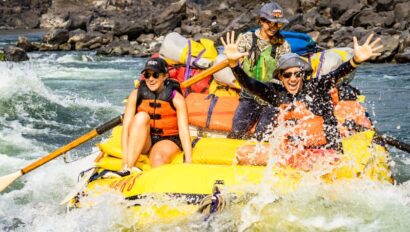 Three people in a yellow raft going through a rapid on the Lower Salmon River with big smiles on their faces.