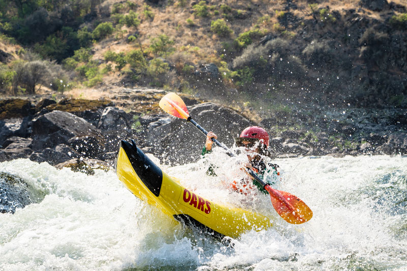 A person wearing a helmet and PFD paddles an yellow inflatable kayak  through a whitewater rapid on the Salmon River