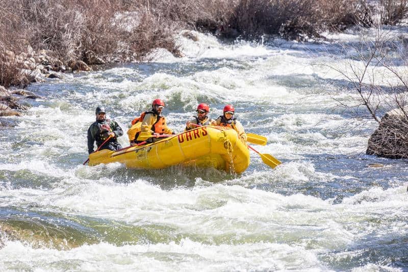 A yellow raft full of people paddles a swift current on the Merced River near Yosemite