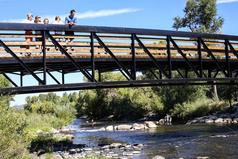 A family stands on a brdge overlooking a river on the Yampa River Core Trail