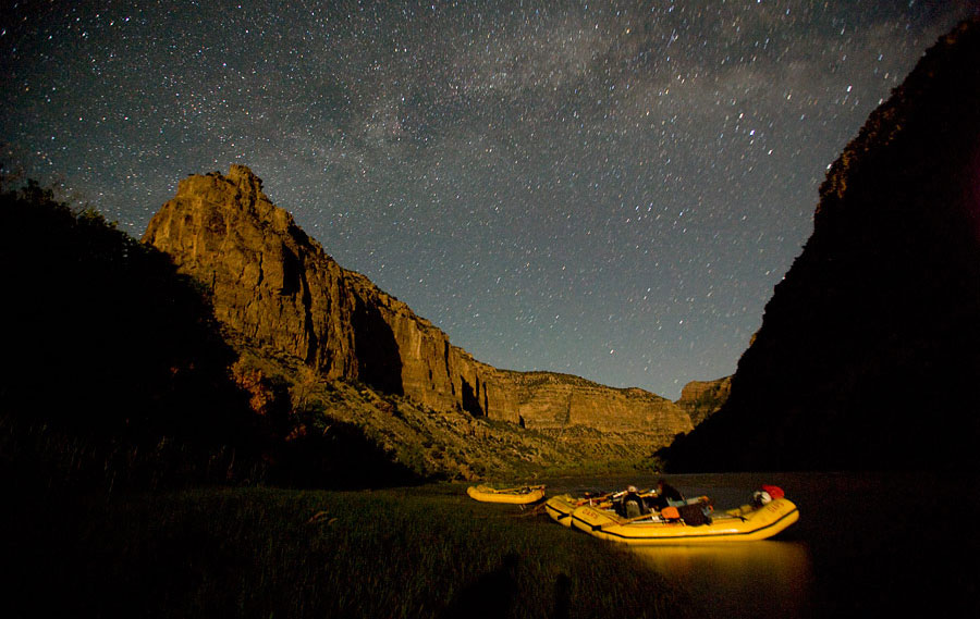 Three yellow rafts tied to shore on the Yampa River beneath a starry night sky
