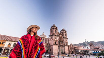 Woman wearing Peruvian blanket stands in front of a building in Cusco, Peru