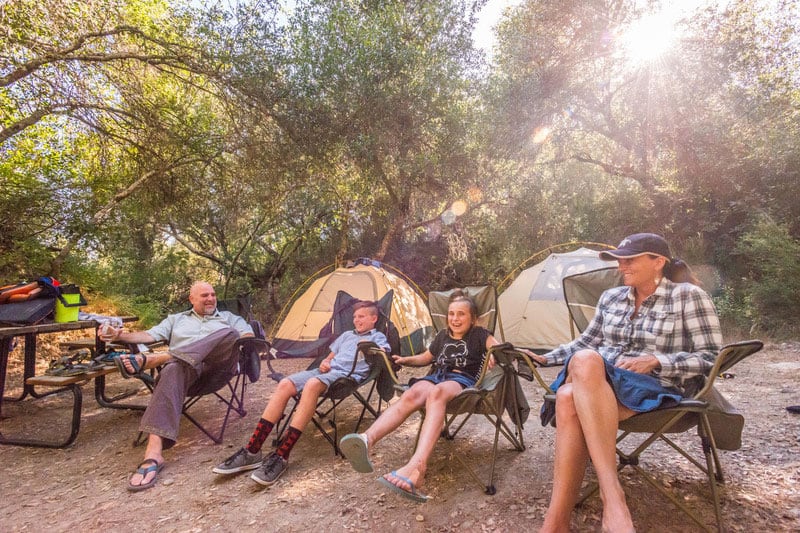 A family sitting in camp chairs in front of their tents at OARS American River Outpost