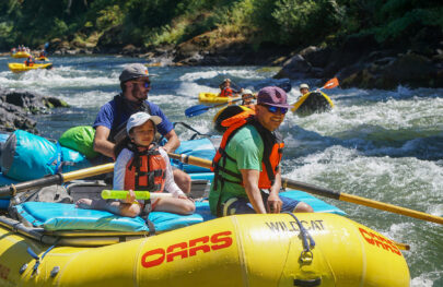 Asian American father and daughter aboard a yellow OARS raft on the Rogue River in Oregon