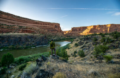 A man in a green shirt looks at the river from above as the sun lights the canyon walls of Westewater Canyon, UT