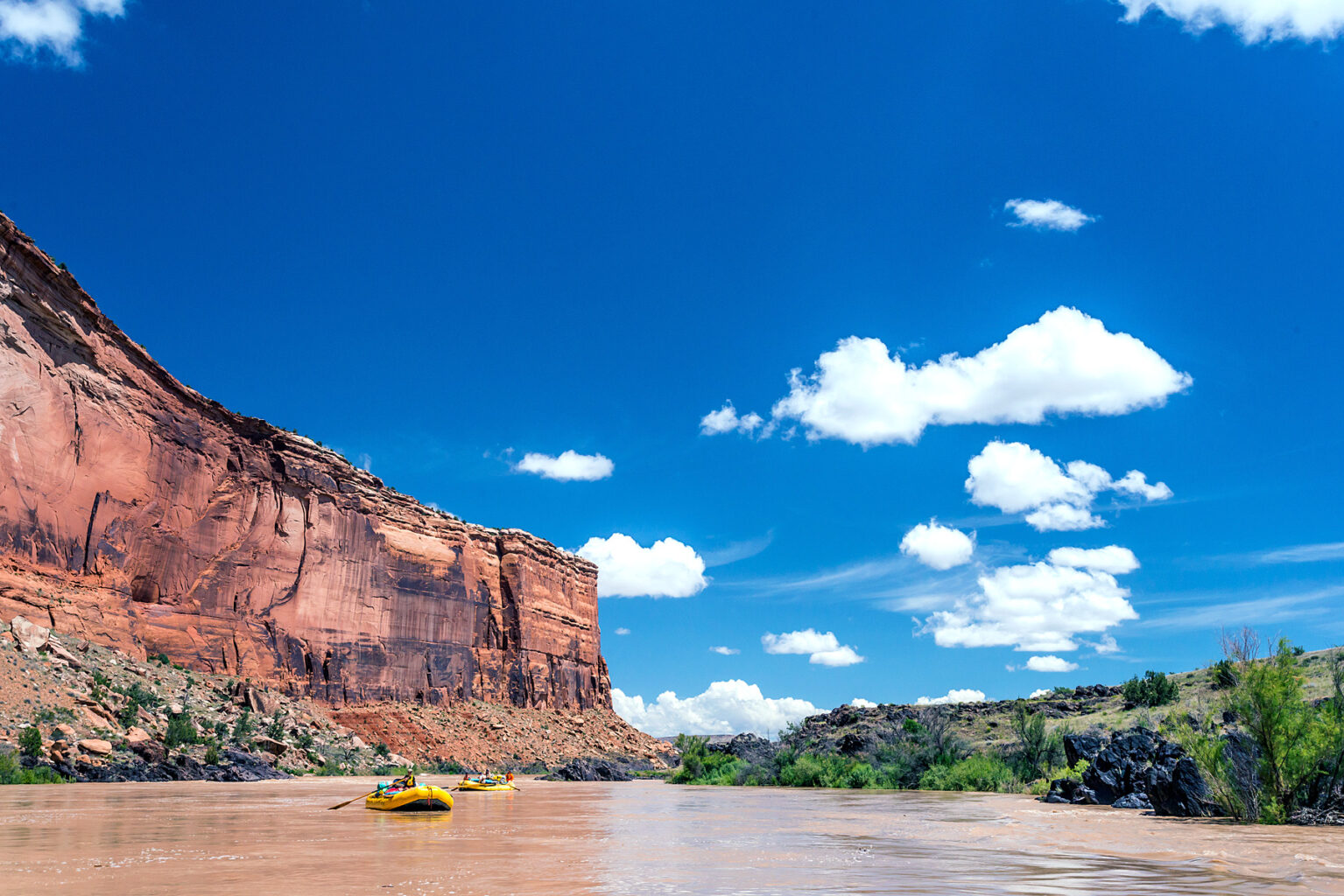 Two rafts in a calm section of Westwater Canyon with red rock cliffs in the background and blue sky on the Colorado River in Utah with OARS