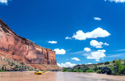 Two rafts in a calm section of Westwater Canyon with red rock cliffs in the background and blue sky on the Colorado River in Utah with OARS