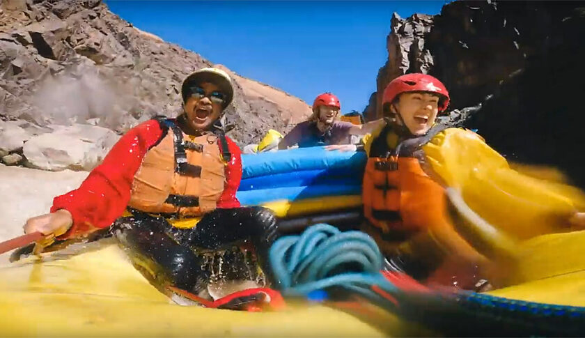 Still image from Westwater Canyon rafting trip with OARS shows happy couple laughing in whitewater with guide in background