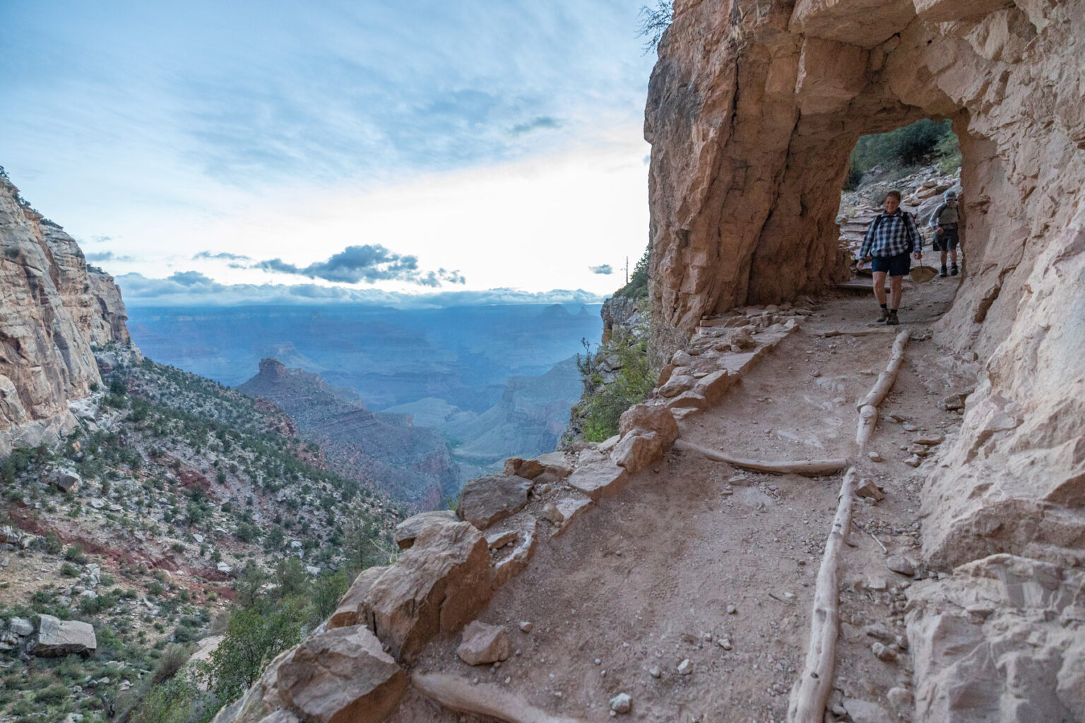 Hikers walk towards camera along Bright Angel Trail with the Grand Canyon off in the distance