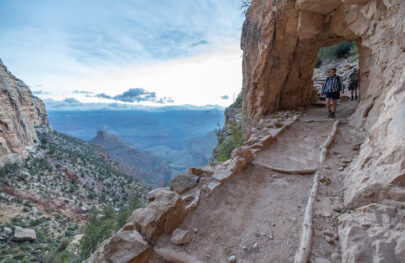 Hikers walk towards camera along Bright Angel Trail with the Grand Canyon off in the distance