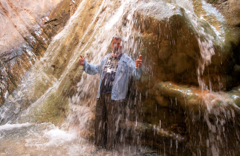 Man stands under waterfall and gives thumbs up in Grand Canyon
