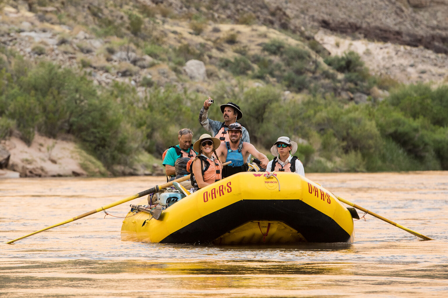 OARS guide rows raft with four guests smiling and taking pictures