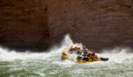 OARS raft hits rapid sending spray up in contrast to dark canyon walls