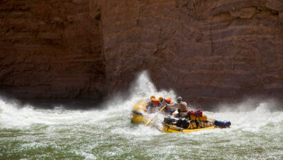 OARS raft hits rapid sending spray up in contrast to dark canyon walls