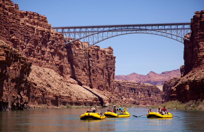 Three yellow OARS rafts travel under bridge near put in at Lees Ferry in Grand Canyon