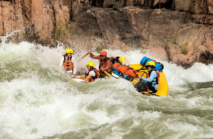 Guide navigates OARS raft through big water with smiling guests in Grand Canyon