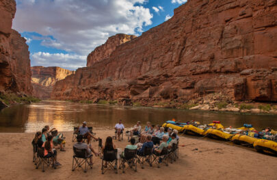 guides and guests in a chair circle on a sandy beach in Grand Canyon with five OARS rafts docked and staked for the night