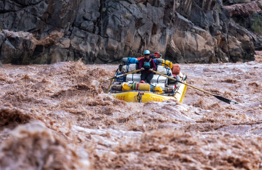 OARS baggage raft navigating muddy rapids in Grand Canyon.