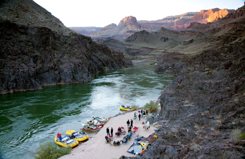 OARS camp from above in Grand Canyon showing moored boats, chair circle, kitchen and tents at sunset