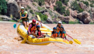 Three ecstatic children in the front of a paddle raft with two adults and a guide behind them as they paddle through a small rapid on the Green River.