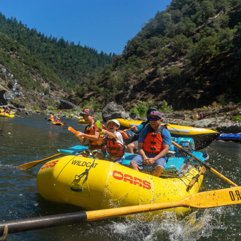 Family having fun with water guns while rafting on a river.