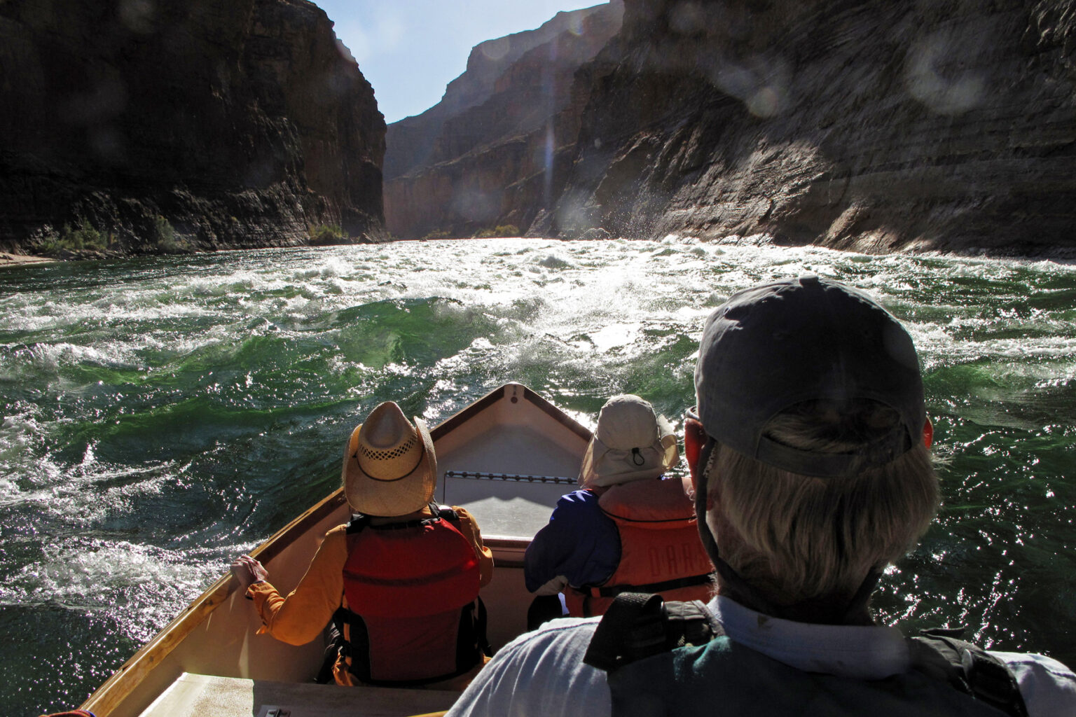 The sun reflects off the top of rapids as an OARS dory heads into turbulent waters in Grand Canyon