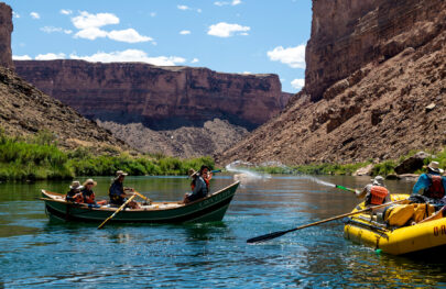Waterfight between guests in an OARS dory and a yellow OARS raft in a calm section of the Colorado River in Grand Canyon