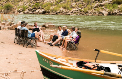 OARS guests chat in a chair circle and the edge of the Colorado River with a dory in the foreground