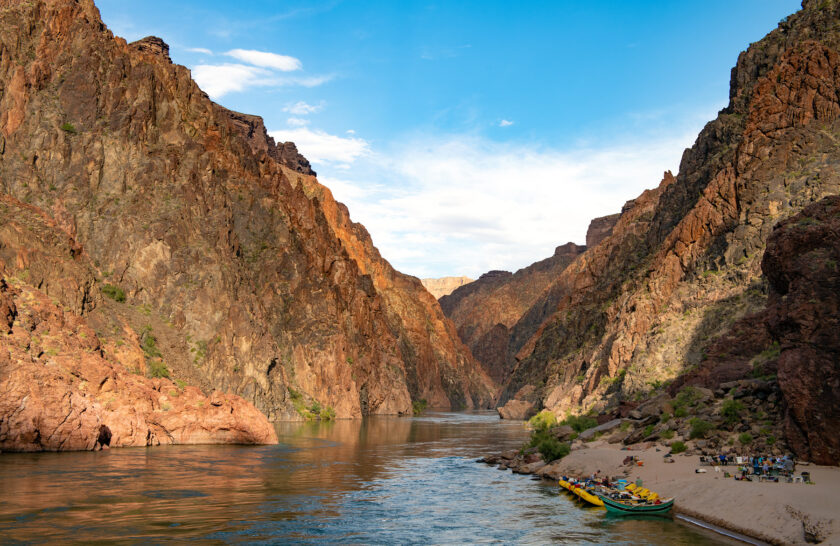 OARS rafts and dory moored at a sandy beach on a calm section of the Grand Canyon with guides and guests relaxing around a chair circle