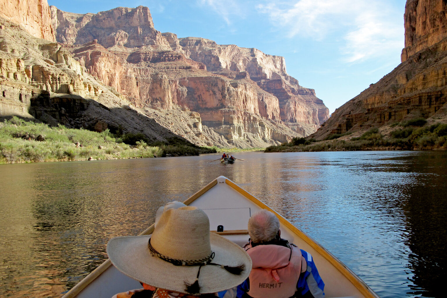 Colorado River looking like a lake with OARS dories rowing towards sunlit cliffs in Grand Canyon