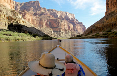 Colorado River looking like a lake with OARS dories rowing towards sunlit cliffs in Grand Canyon