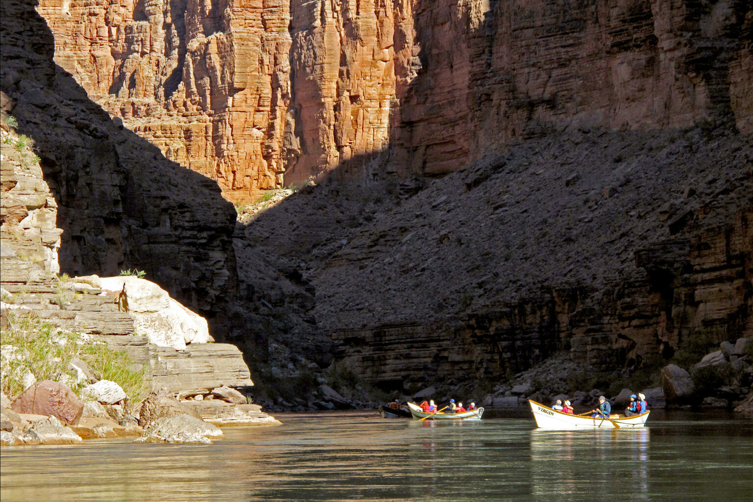 OARS dories are lit by sunlight against the cliffs in shadow deep in Grand Canyon