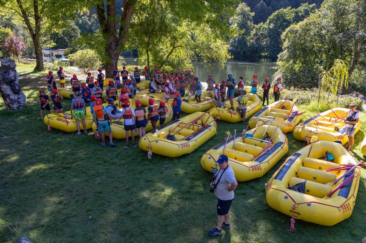 A group of rafters gathers around a fleet of yellow rafts while listening to river guides provide helpful information