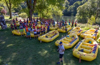 A group of rafters gathers around a fleet of yellow rafts while listening to river guides provide helpful information