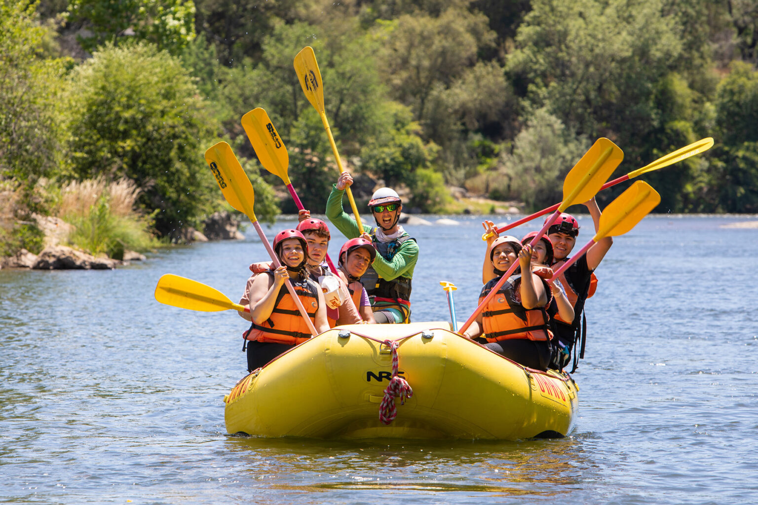 A group rafting on the South Fork of the American River raises their paddles.