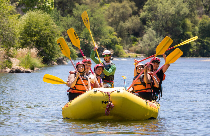 A group rafting on the South Fork of the American River raises their paddles.