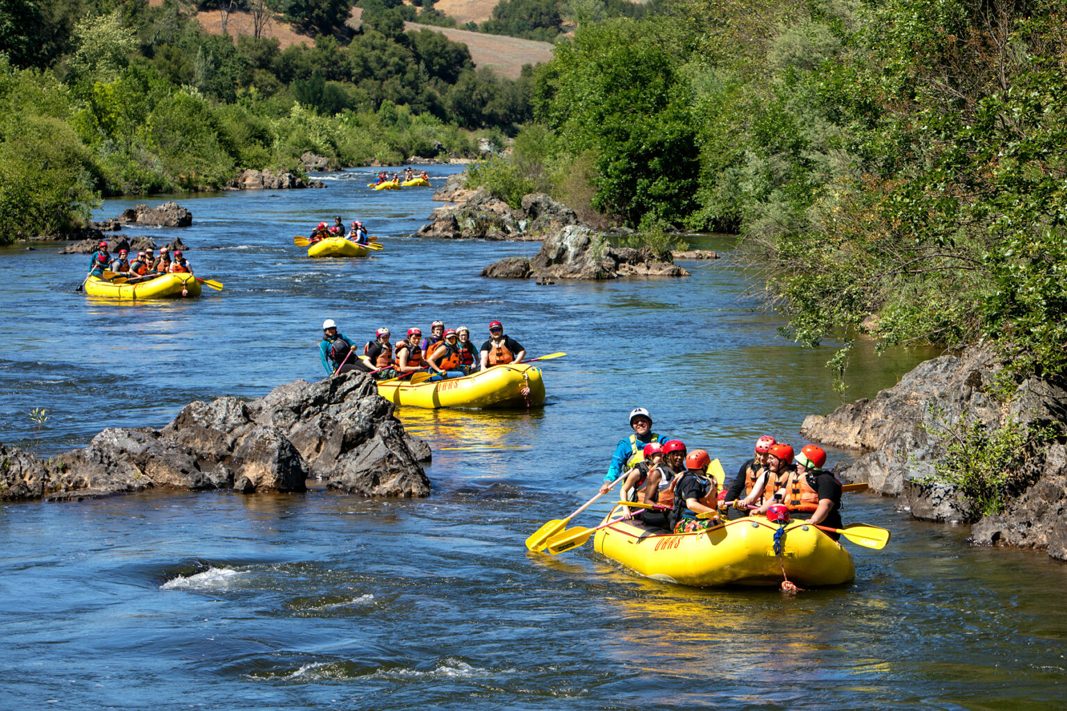 Several yellow rafts full of paddlers spread out on the South Fork of the American River in California